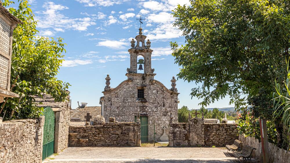 A historic stone church with a bell tower, surrounded by cobblestone streets and greenery.