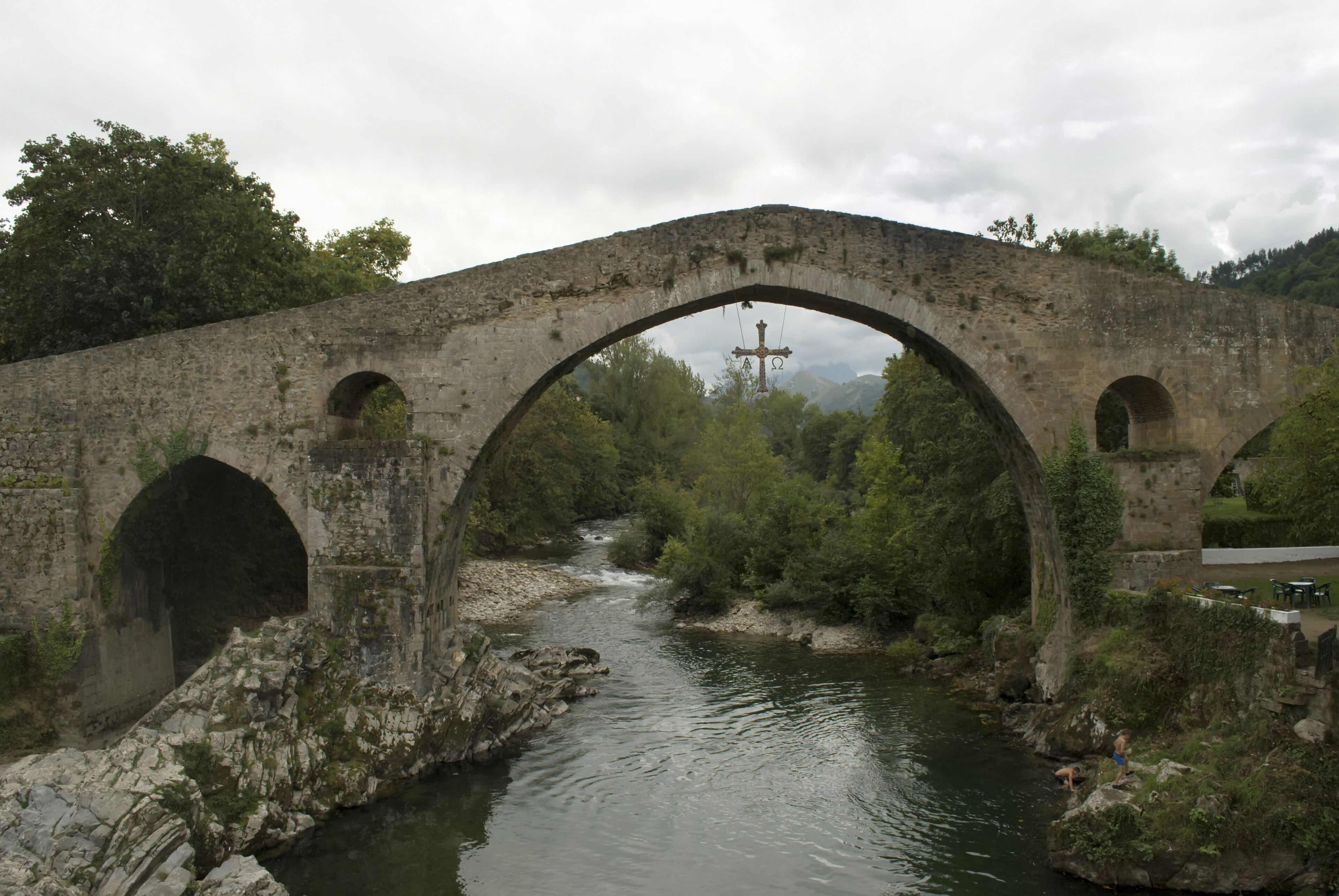 An old stone bridge over a river with a cross in the background.