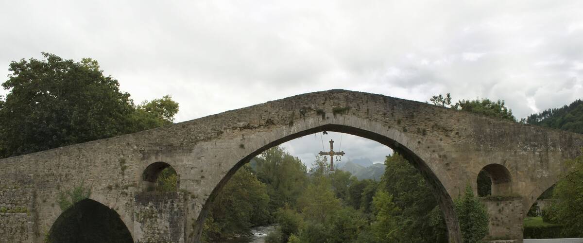 An old stone bridge over a river with a cross in the background.
