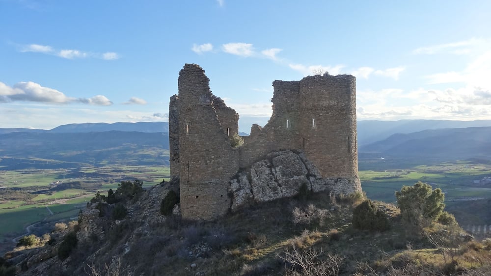 Ein zerfallener SteinTurm auf einem Hügel, mit einem Tal und Bergen im Hintergrund.