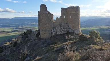 A ruined stone tower on a hill with a valley and mountains in the background.