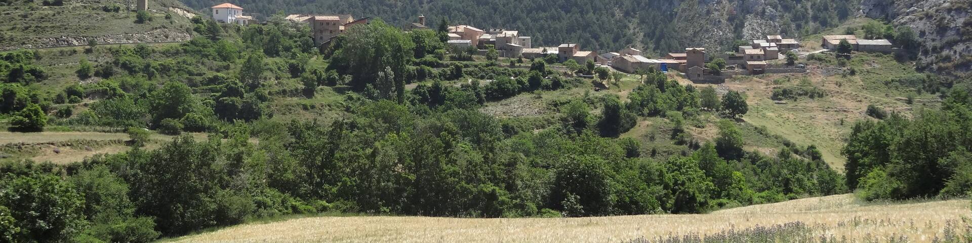A rural landscape with a village nestled among green hills and a prominent mountain in the background.
