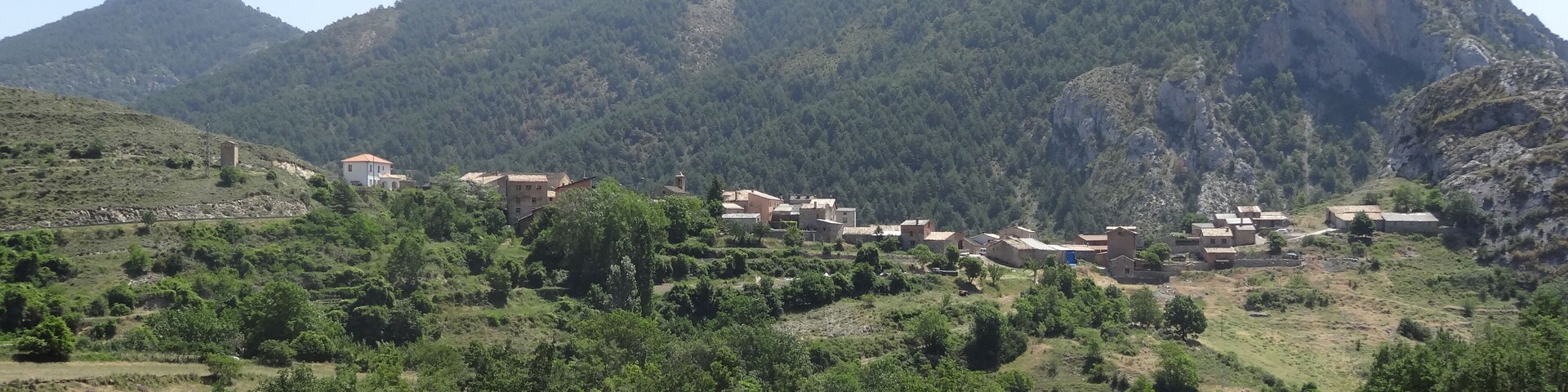 Paisaje rural con un pueblo enclavado entre colinas verdes y una montaña destacada al fondo.