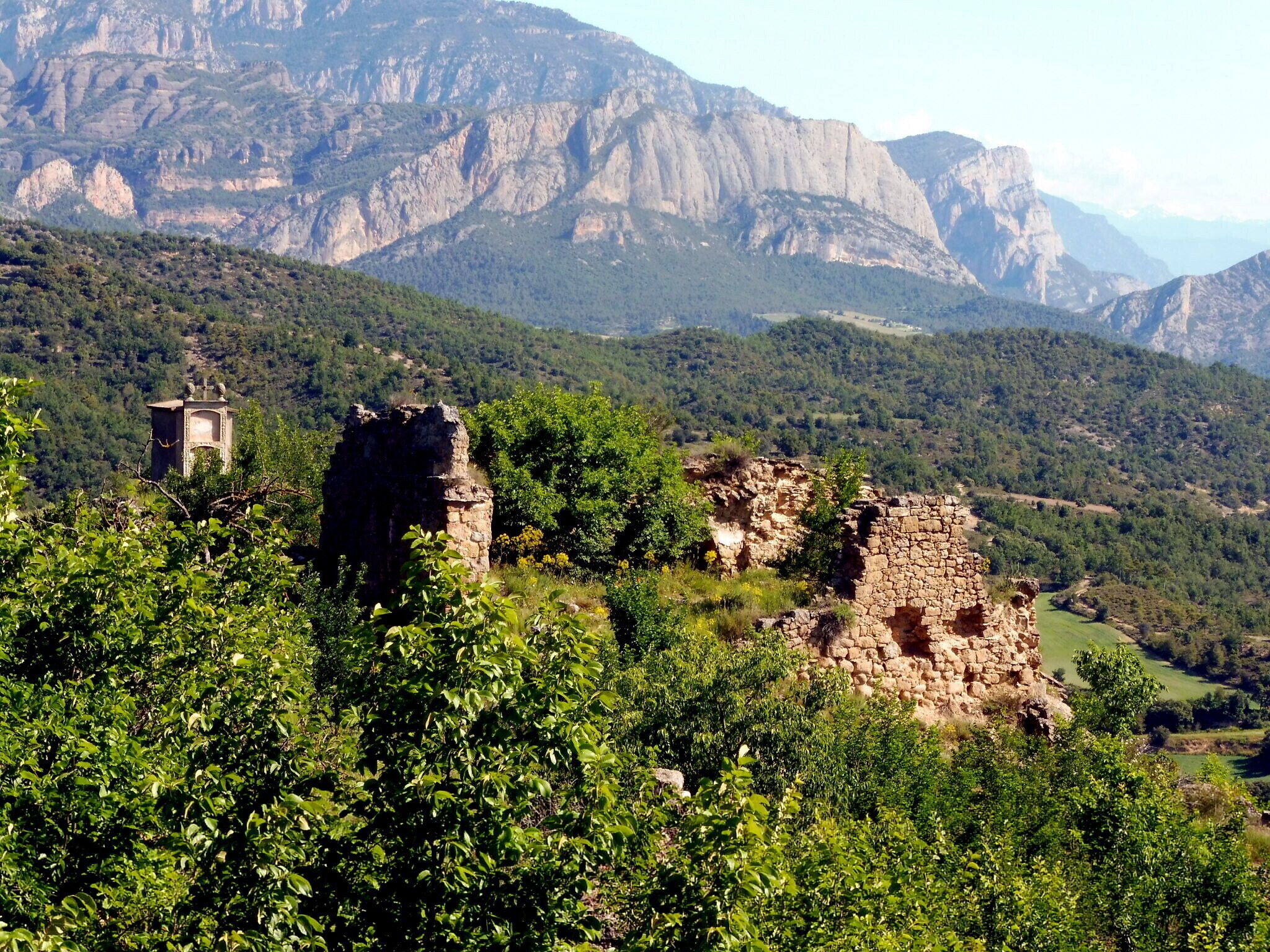 A mountainous landscape with ancient stone ruins and a small tower amidst lush greenery.