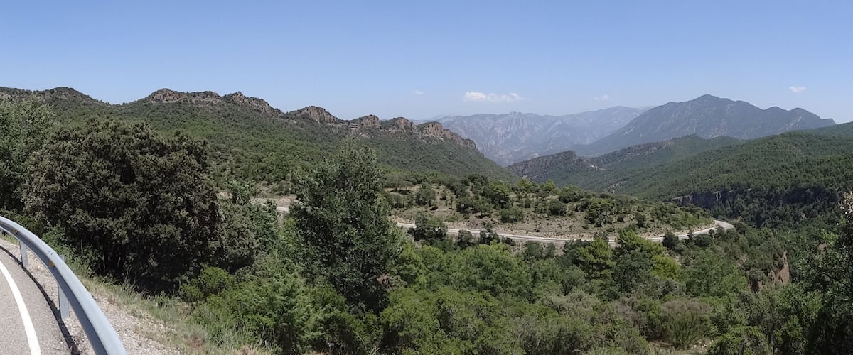 A winding mountain road flanked by dense forests and rugged hills.