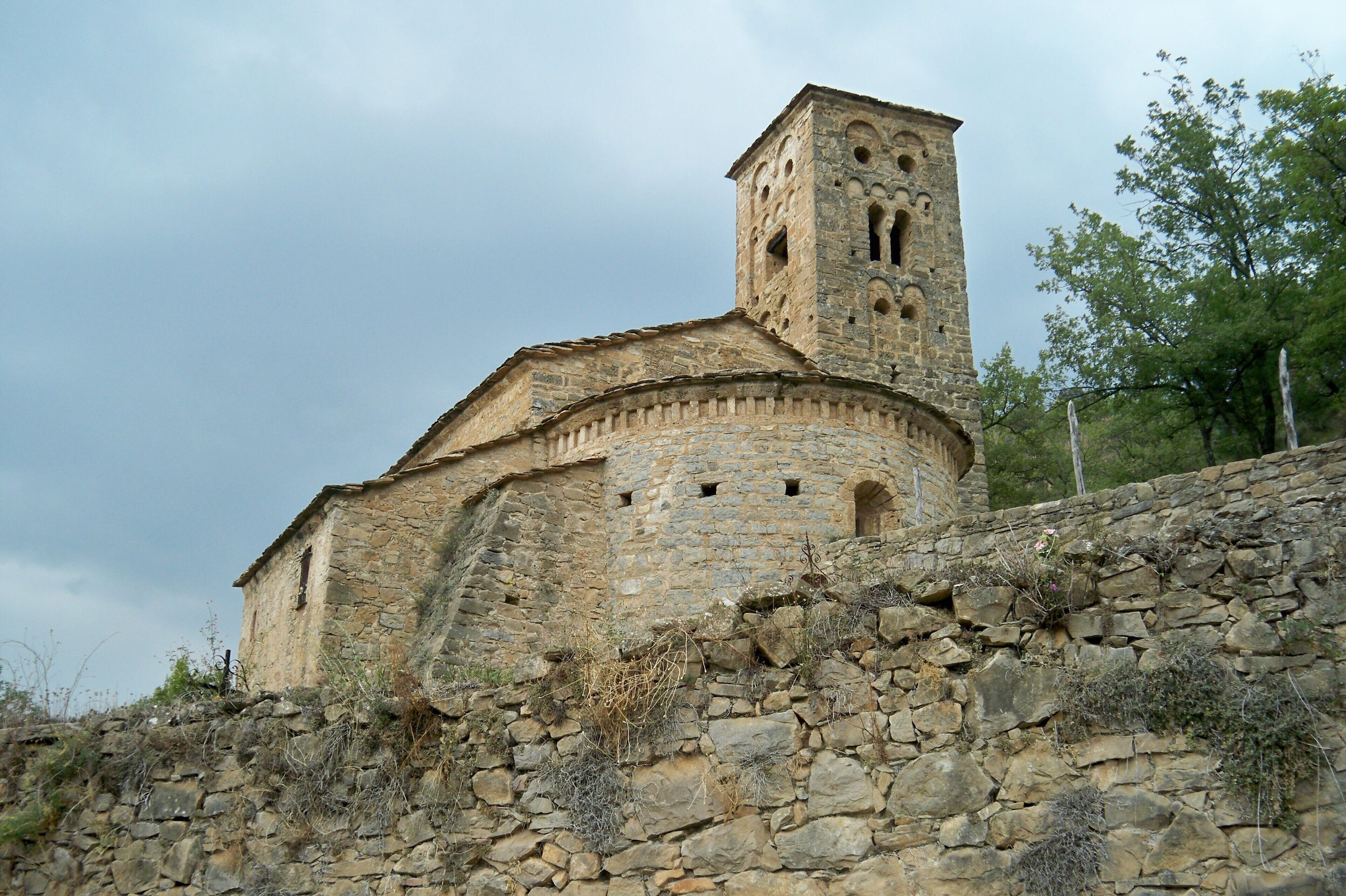 A stone church with a bell tower, surrounded by a stone wall and trees.