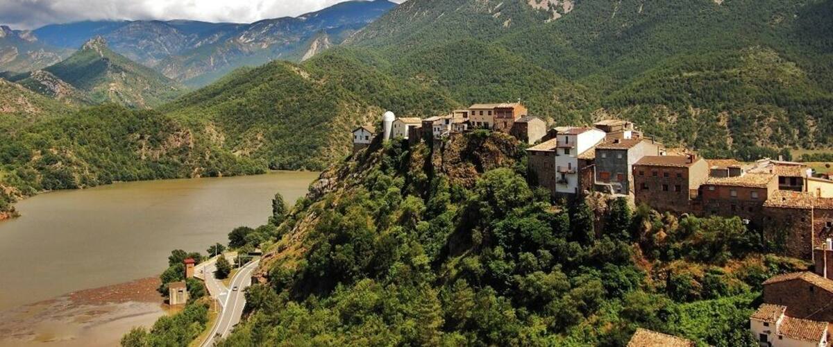 A mountainous landscape with a village perched on a hill overlooking a river.