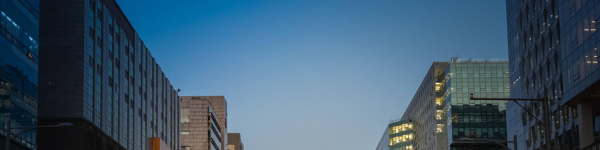 Early evening with a full moon, traces of people busily crossing the street between tall buildings (South Korea, Seongnam, Pangyo Techno valley)