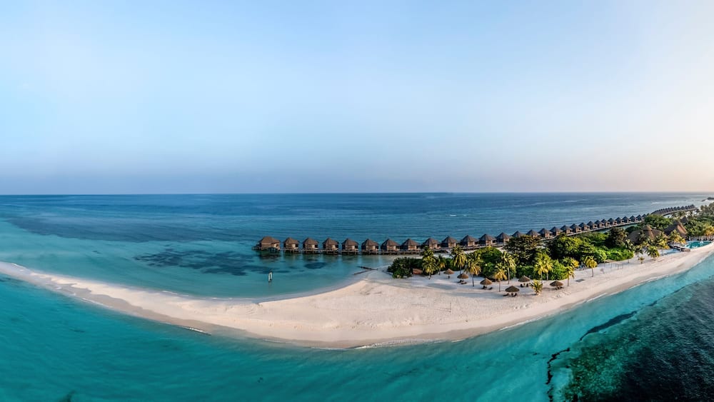 Maldives, Lhaviyani Atoll, Kuredu, Aerial panorama of coastal beach and row of resort bungalows surrounded by waters of Indian Ocean at sunrise