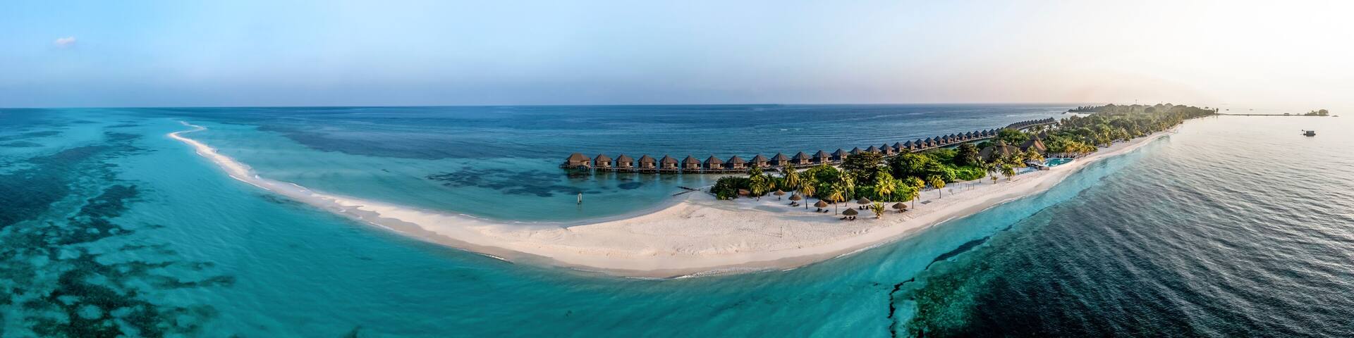 Maldives, Lhaviyani Atoll, Kuredu, Aerial panorama of coastal beach and row of resort bungalows surrounded by waters of Indian Ocean at sunrise
