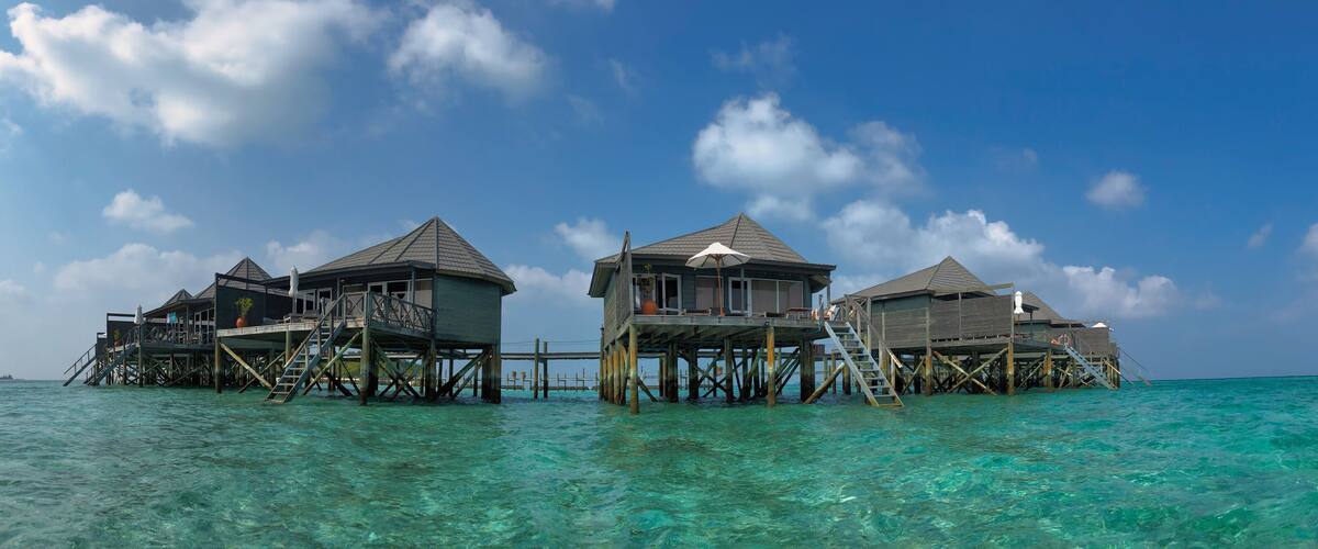 Scenic Panorama of Wooden Water Villa in Maldivian Resort. Overwater Bungalow with Turquoise Lagoon of Laccadive Sea and Blue Sky with Clouds in Maldives.