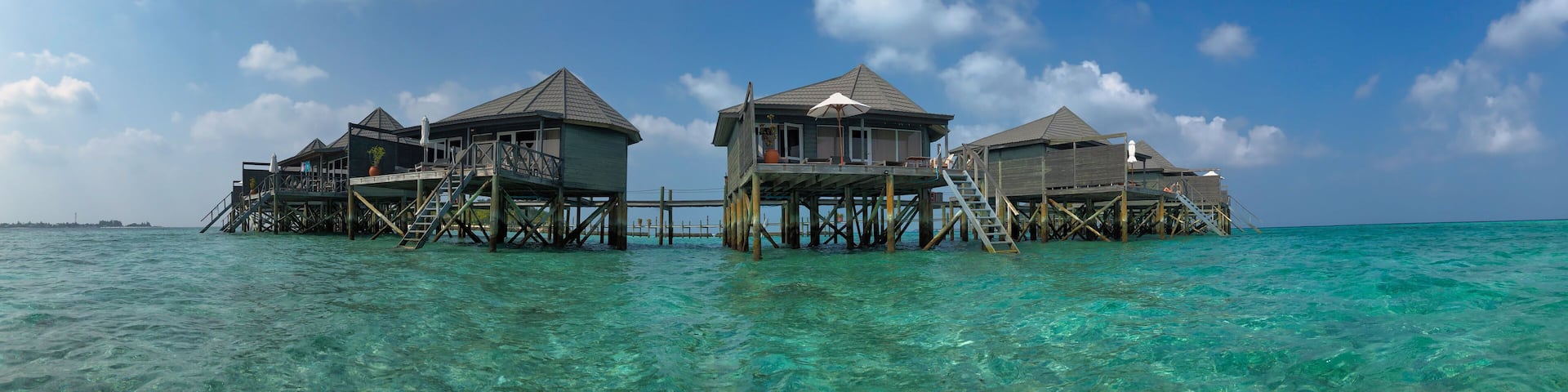 Scenic Panorama of Wooden Water Villa in Maldivian Resort. Overwater Bungalow with Turquoise Lagoon of Laccadive Sea and Blue Sky with Clouds in Maldives.