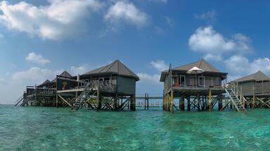 Scenic Panorama of Wooden Water Villa in Maldivian Resort. Overwater Bungalow with Turquoise Lagoon of Laccadive Sea and Blue Sky with Clouds in Maldives.
