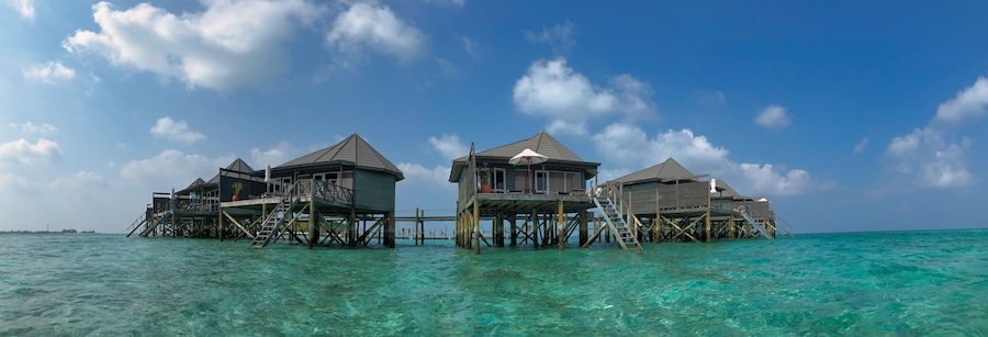 Scenic Panorama of Wooden Water Villa in Maldivian Resort. Overwater Bungalow with Turquoise Lagoon of Laccadive Sea and Blue Sky with Clouds in Maldives.