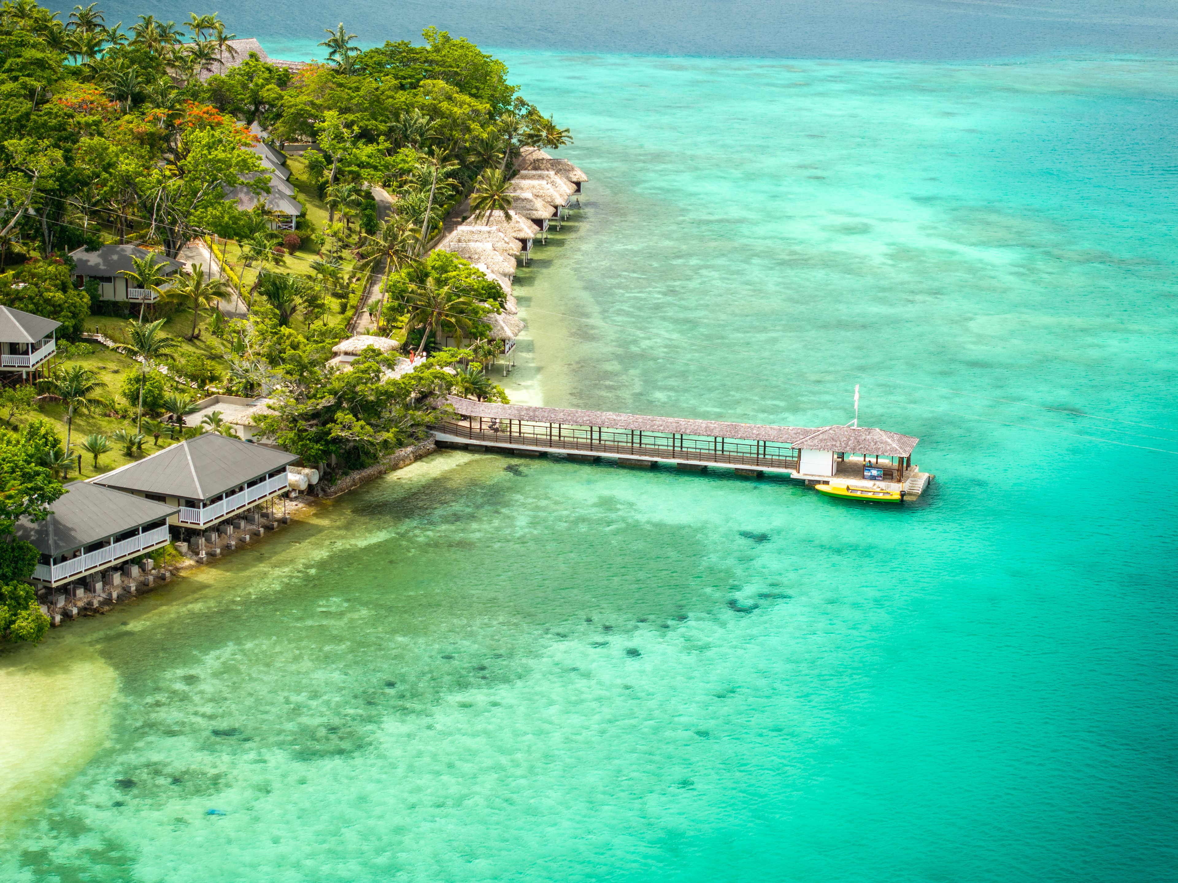 An aerial view of a tropical resort with overwater bungalows, clear turquoise waters, and lush greenery.