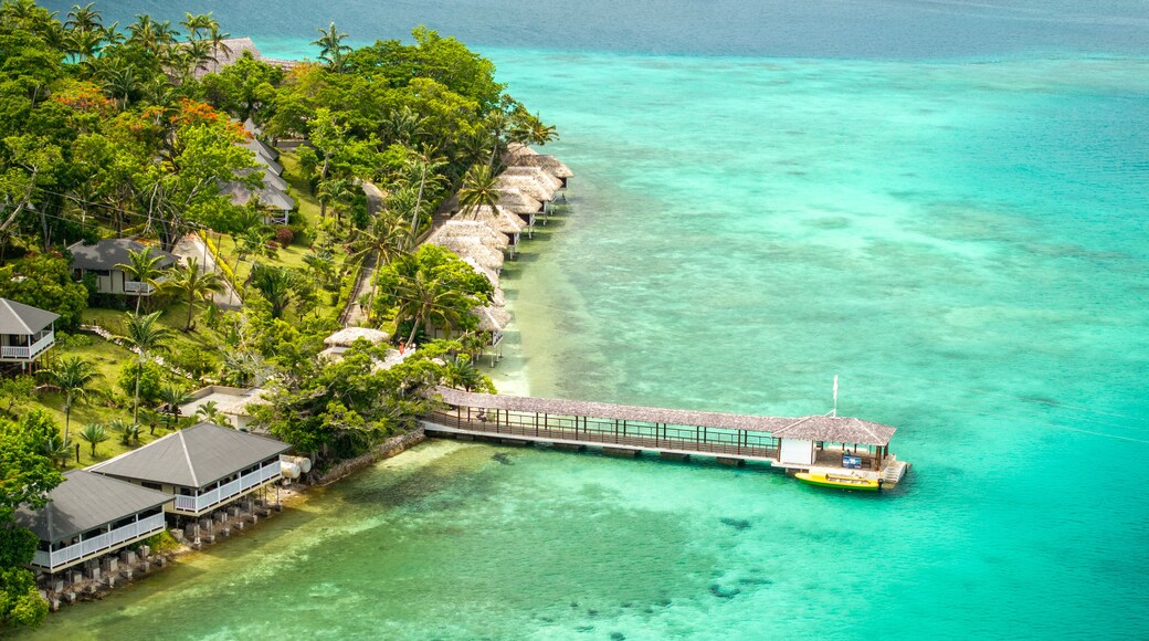 An aerial view of a tropical resort with overwater bungalows, clear turquoise waters, and lush greenery.