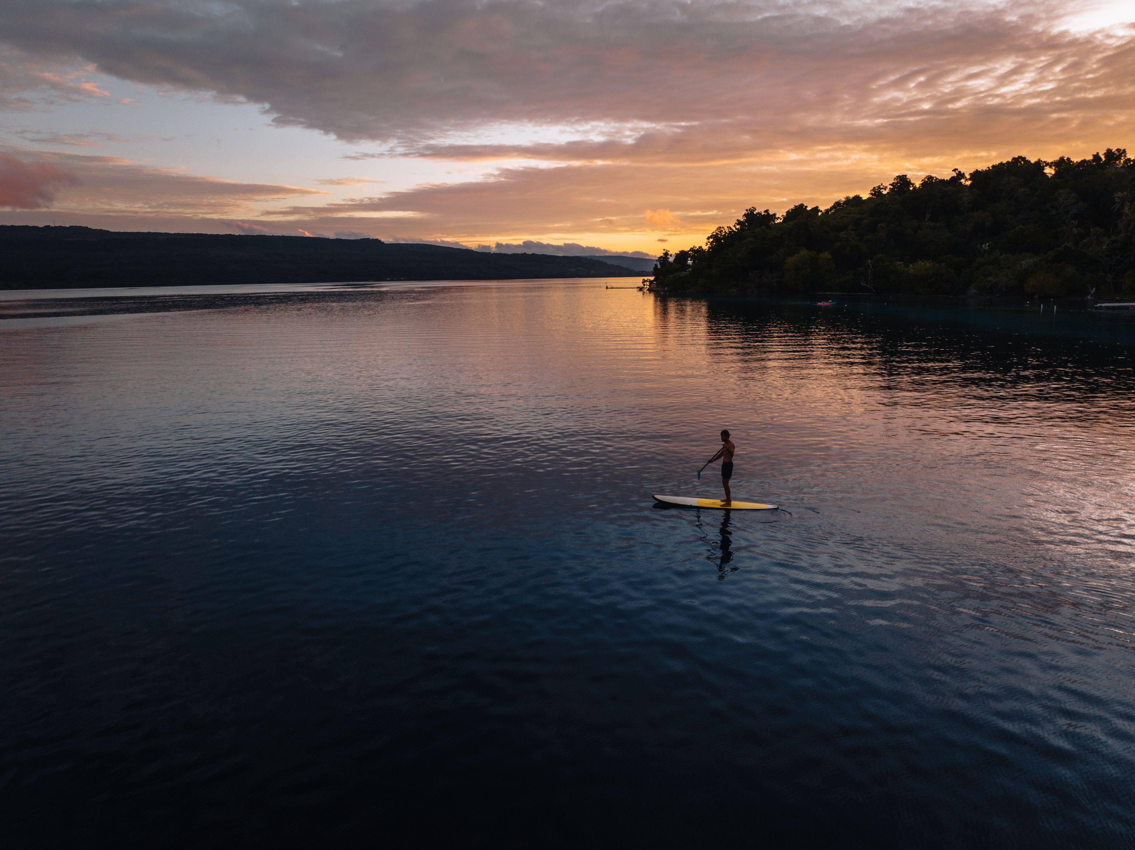 Una persona haciendo paddleboard en un lago tranquilo al atardecer.