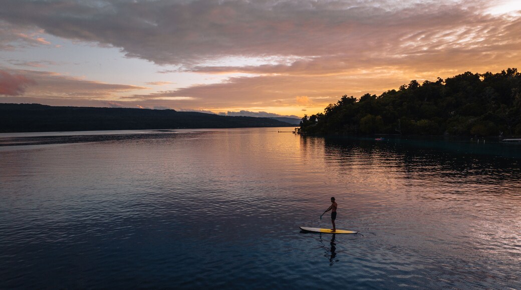 A person paddleboarding on a calm lake at sunset.