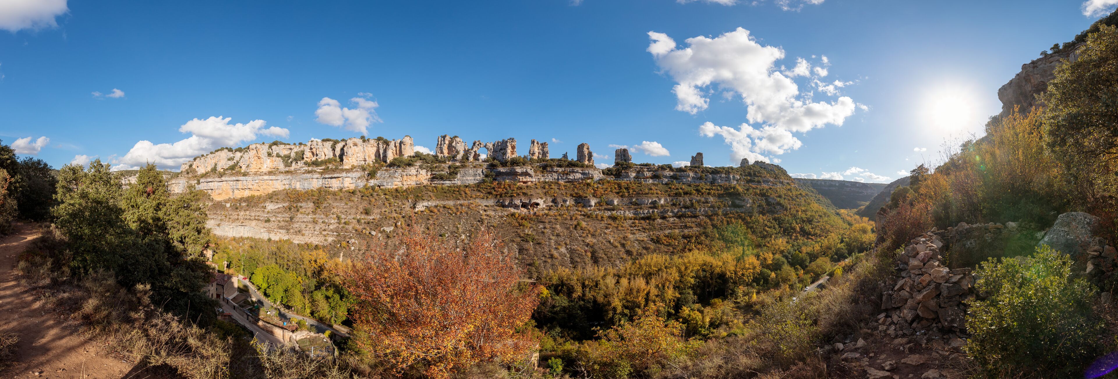 A mountainous landscape with a clear sky, autumn-colored trees, and a winding road.
