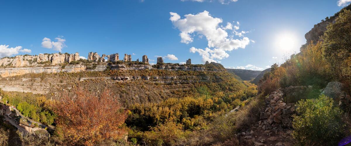 A mountainous landscape with a clear sky, autumn-colored trees, and a winding road.