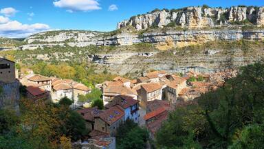A village nestled in a valley with terraced houses and a prominent cliff face in the background.