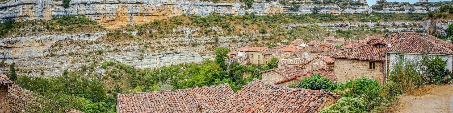 A village with terracotta-roofed houses nestled in a valley, surrounded by rocky cliffs and greenery.
