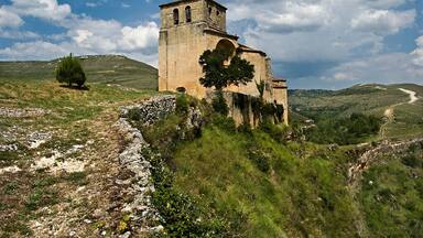 A historic stone church with a bell tower on a grassy hill.