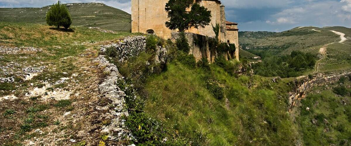 A historic stone church with a bell tower on a grassy hill.