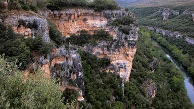 A rugged cliff with a river flowing through a valley surrounded by mountains.