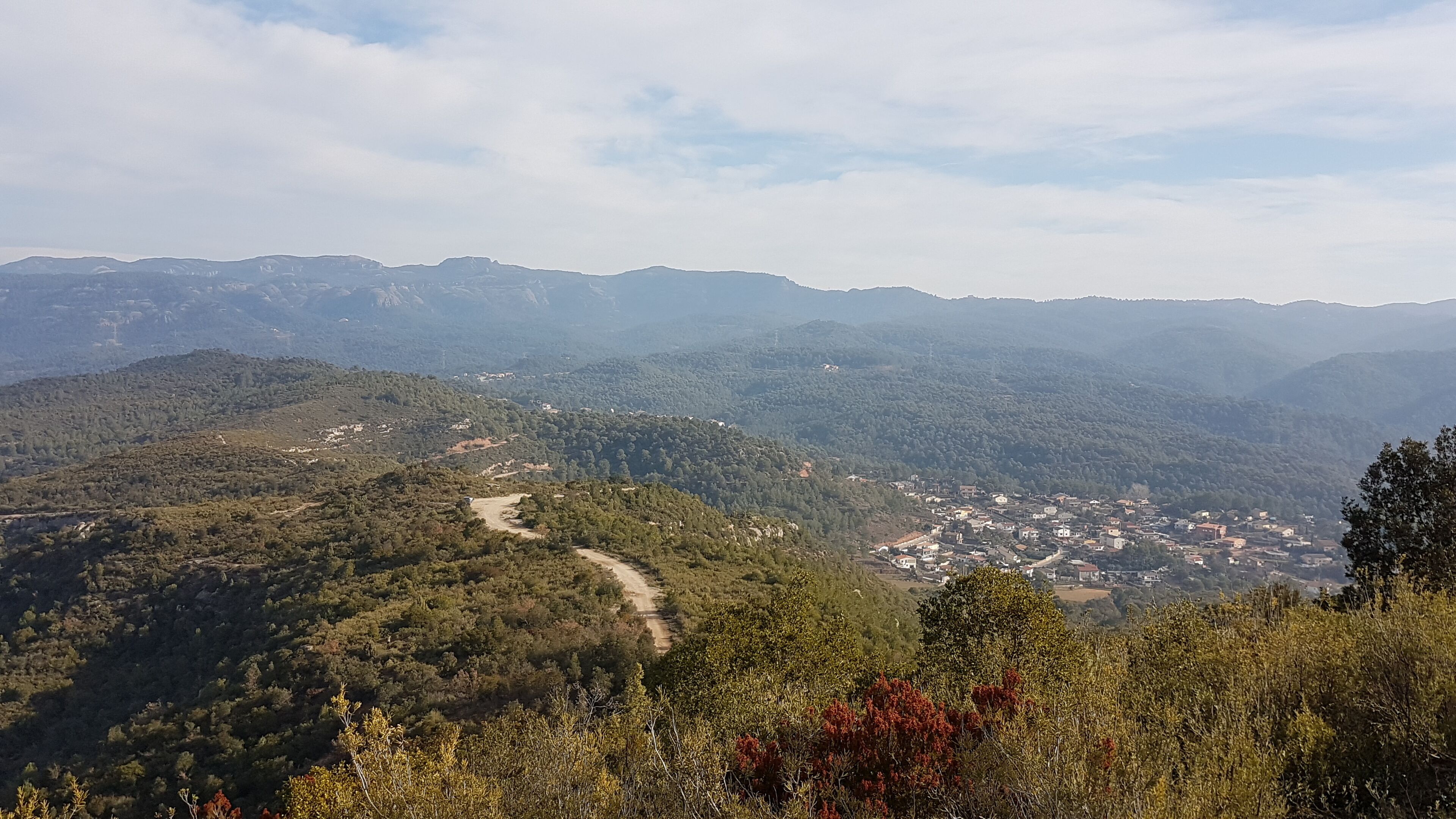 A mountainous landscape with a winding road, dense forests, and a small town nestled in the valley.