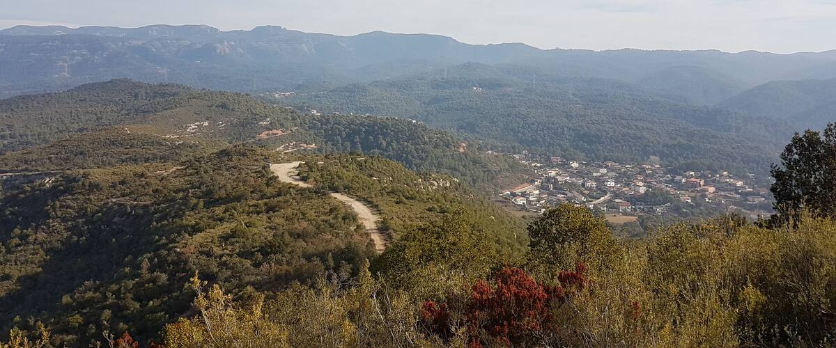 A mountainous landscape with a winding road, dense forests, and a small town nestled in the valley.