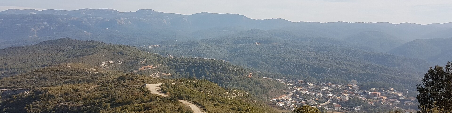 A mountainous landscape with a winding road, dense forests, and a small town nestled in the valley.