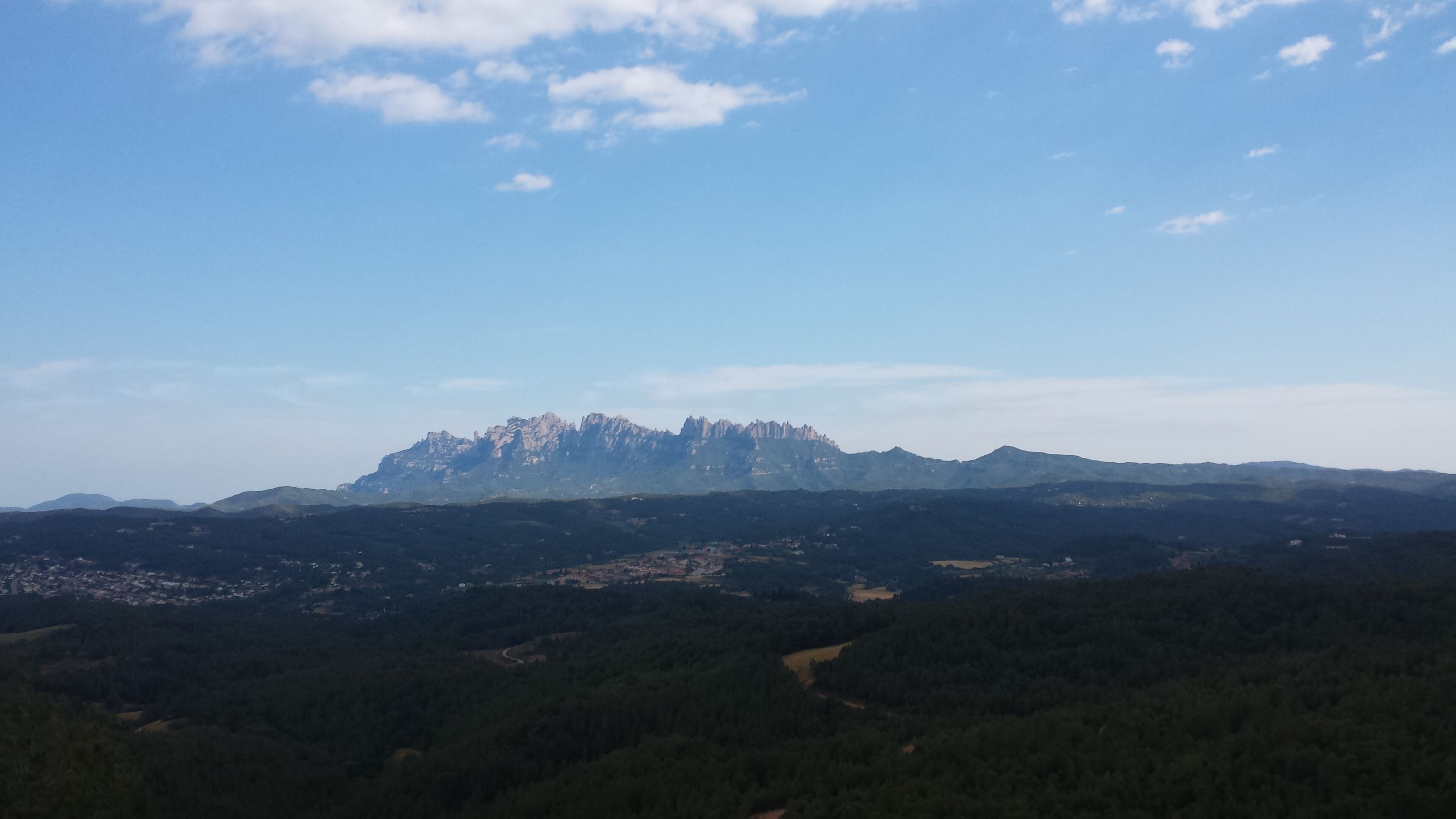 A mountain range with a prominent peak, surrounded by dense forests and a clear sky.