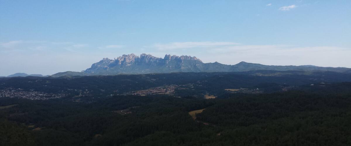 A mountain range with a prominent peak, surrounded by dense forests and a clear sky.