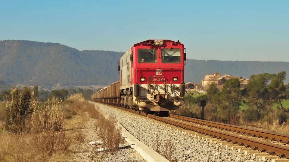 A red train on tracks with a mountainous landscape in the background.