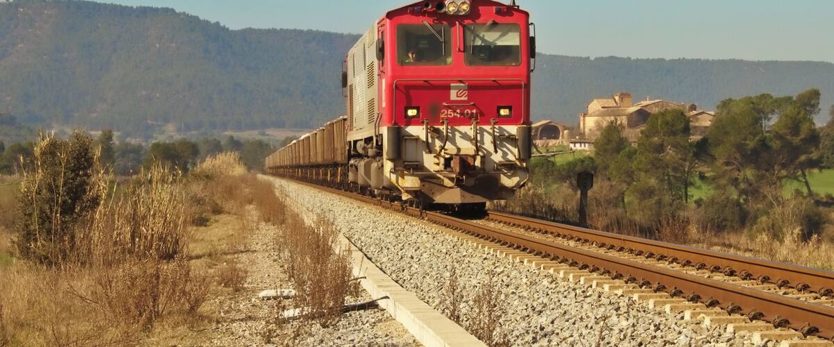 A red train on tracks with a mountainous landscape in the background.