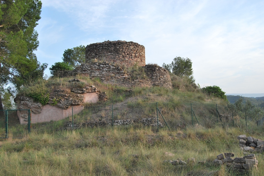 An ancient stone structure on a grassy hill with a fence in the foreground.