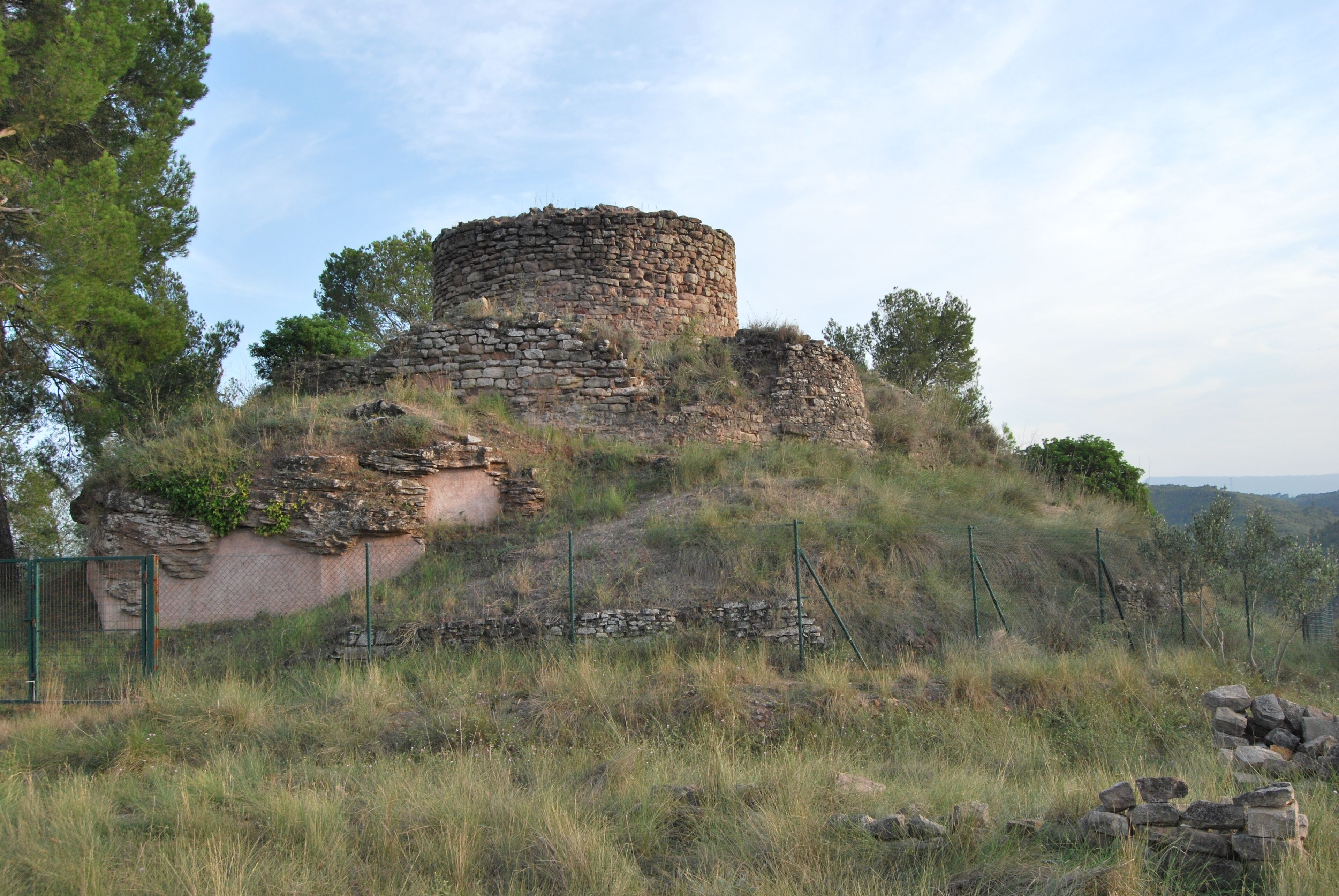 An ancient stone structure on a grassy hill with a fence in the foreground.