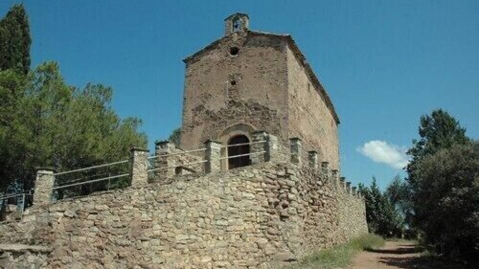 A stone tower with a small arched entrance, surrounded by a stone wall and trees.