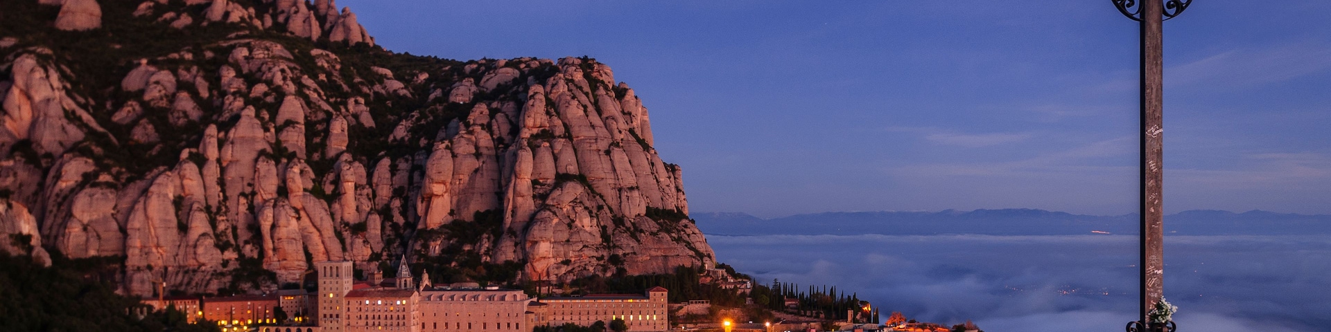 Paisagem montanhosa com um monumento em forma de cruz e um conjunto de edifícios iluminados.