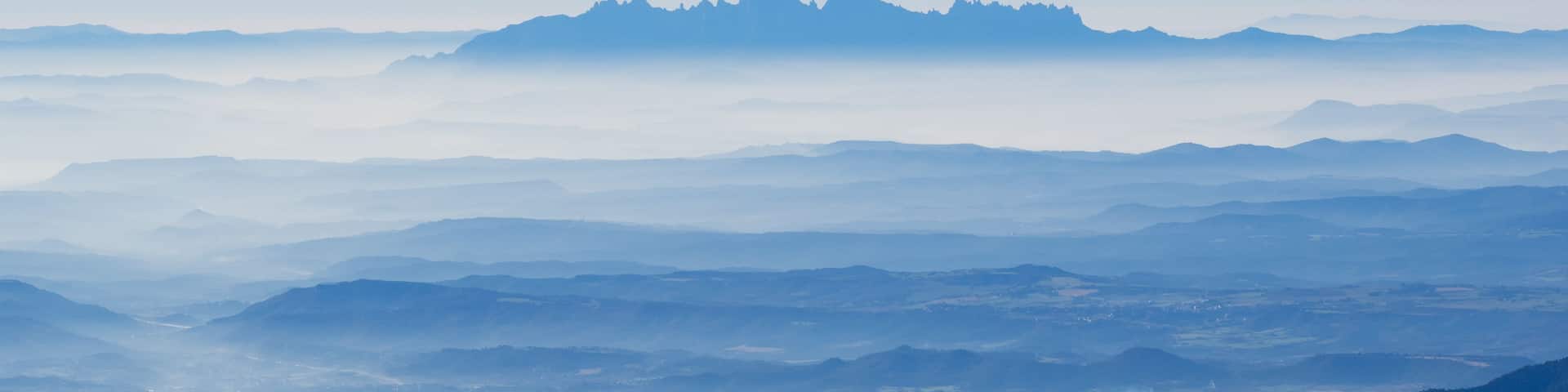 A layered mountain range with a hazy foreground and a clear peak in the distance.