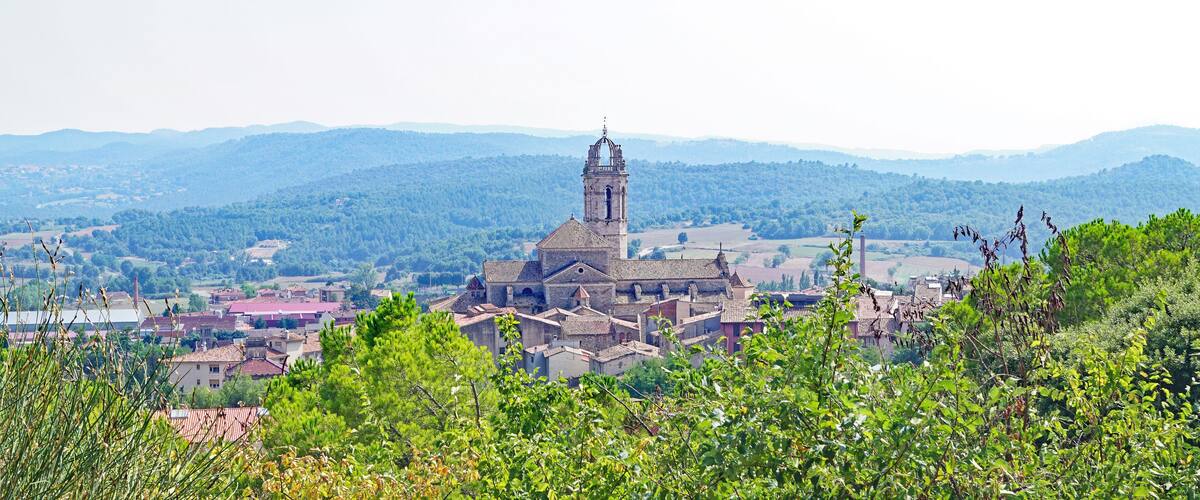 A historic church with a tall bell tower surrounded by lush greenery and rolling hills in the background.