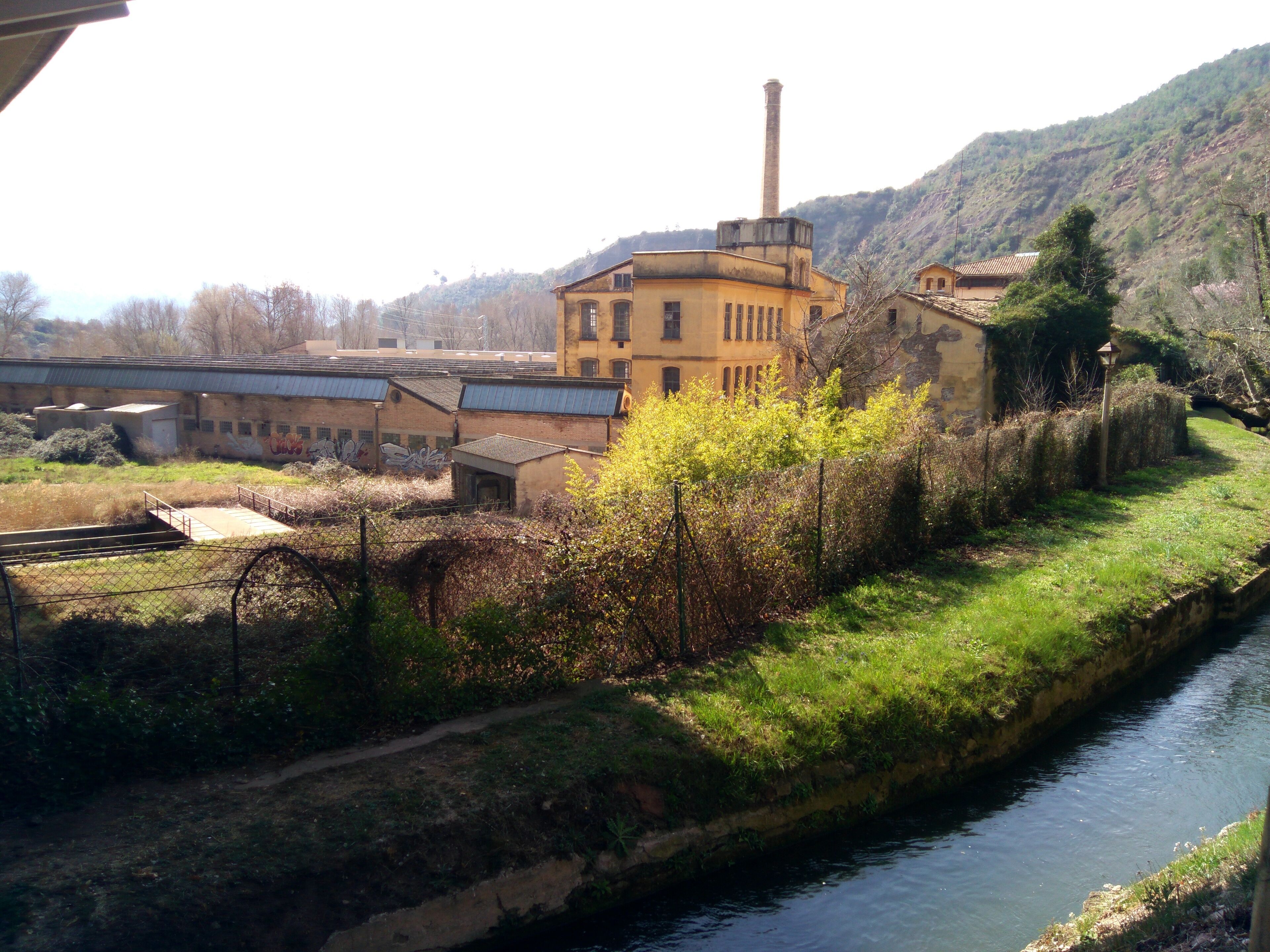A river, a bridge, and industrial buildings with a chimney.