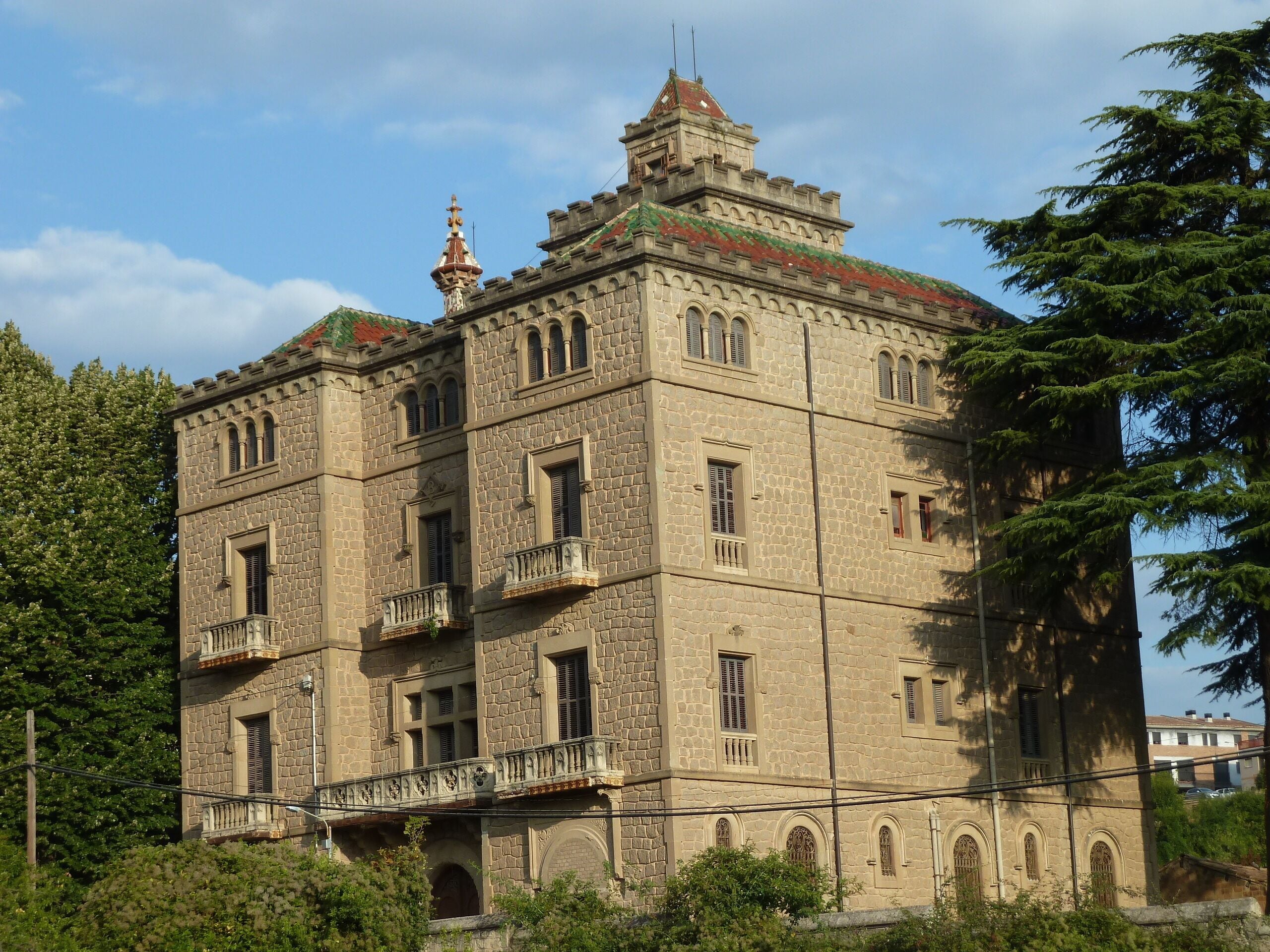 Un edificio grande e histórico de piedra con balcones ornamentales y techo de tejas rojas.