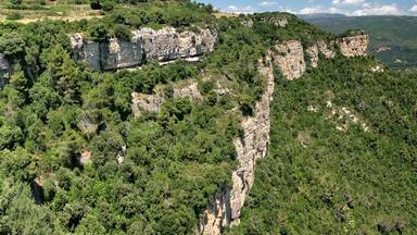 A rugged cliffside with dense green vegetation and a clear sky.