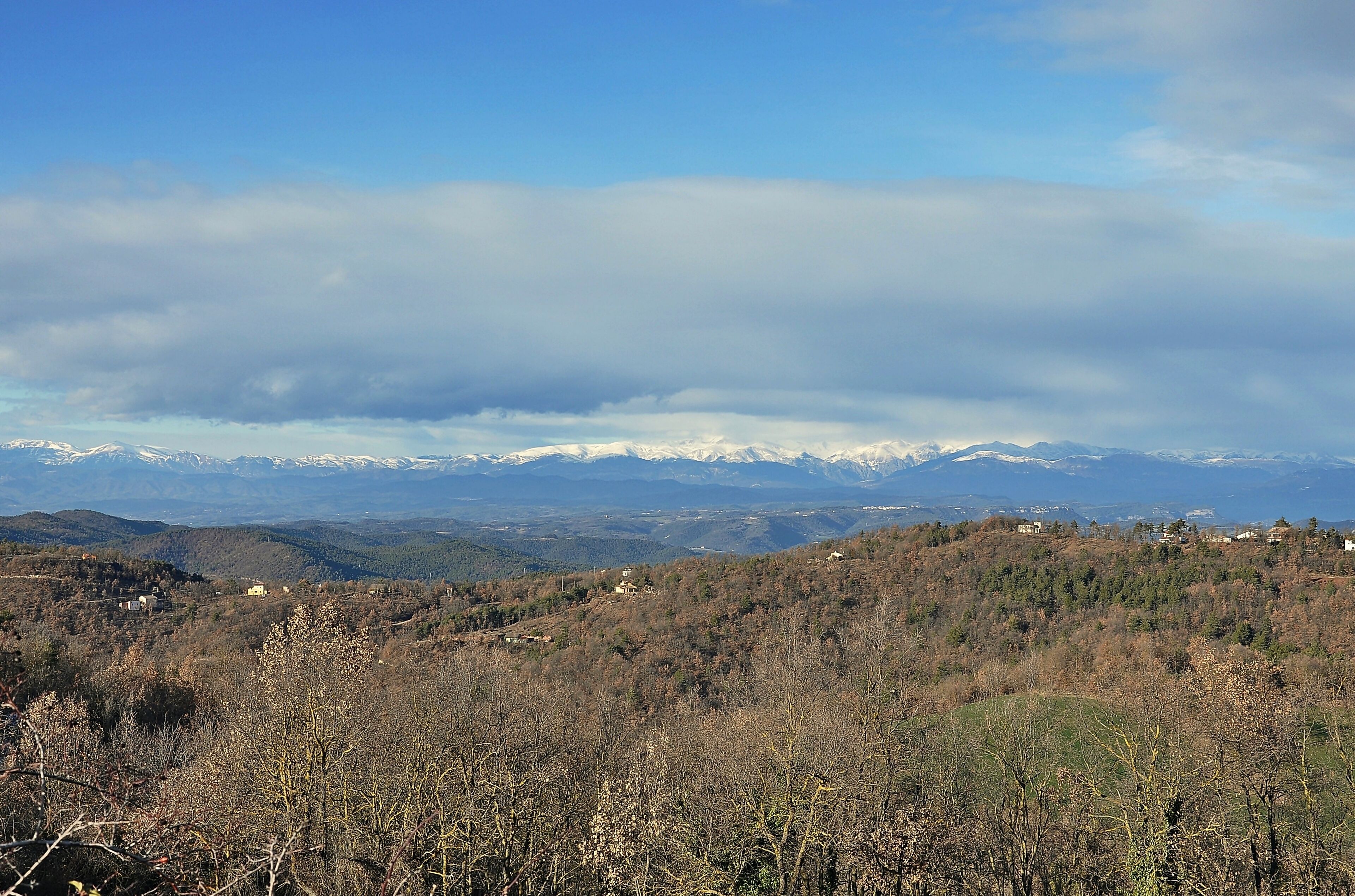 A mountainous landscape with snow-capped peaks, scattered houses, and dense forest.