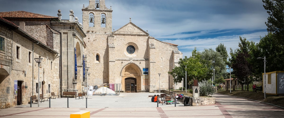 A historic church with a bell tower, a paved square with benches, and surrounding trees.