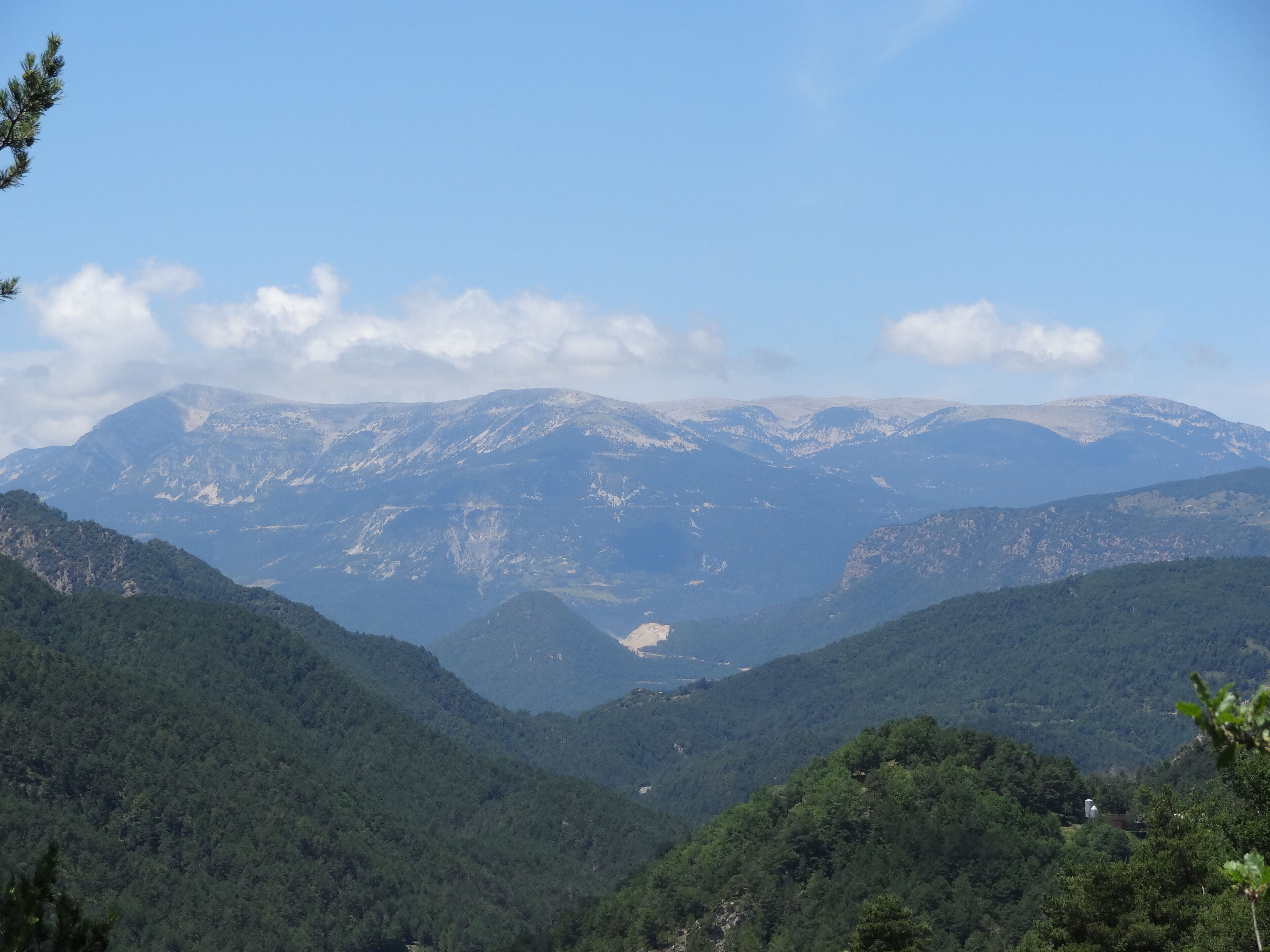 A mountainous landscape with dense forests and snow-capped peaks under a clear sky.