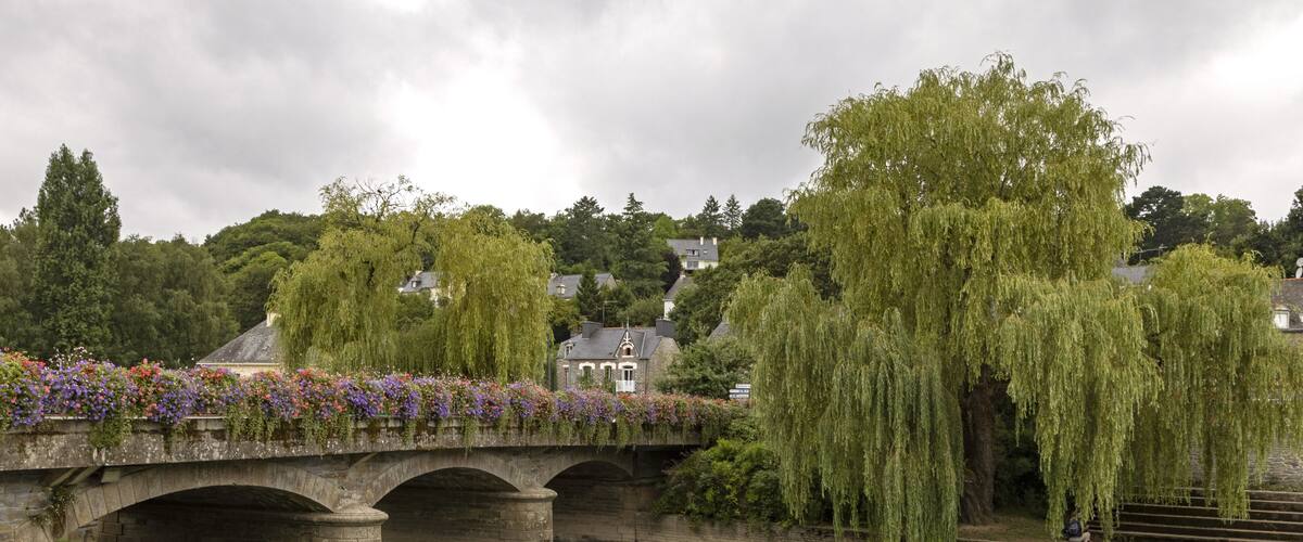 A stone bridge over a river with weeping willow trees and colorful flowers.