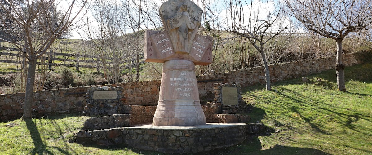 A stone monument with inscriptions, surrounded by a stone wall and trees.